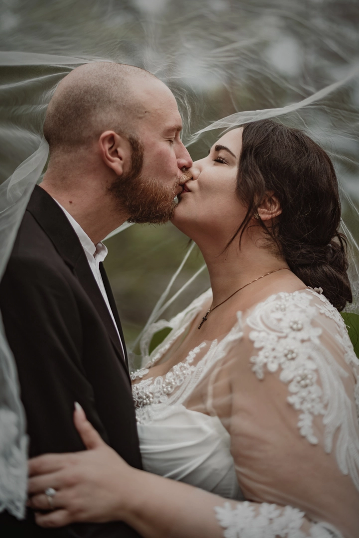 Wedding photographer Stockholm documents newlywed couple kissing under the brides vail draping over them